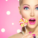 Funny girl eating lollipop over pink polka dots background